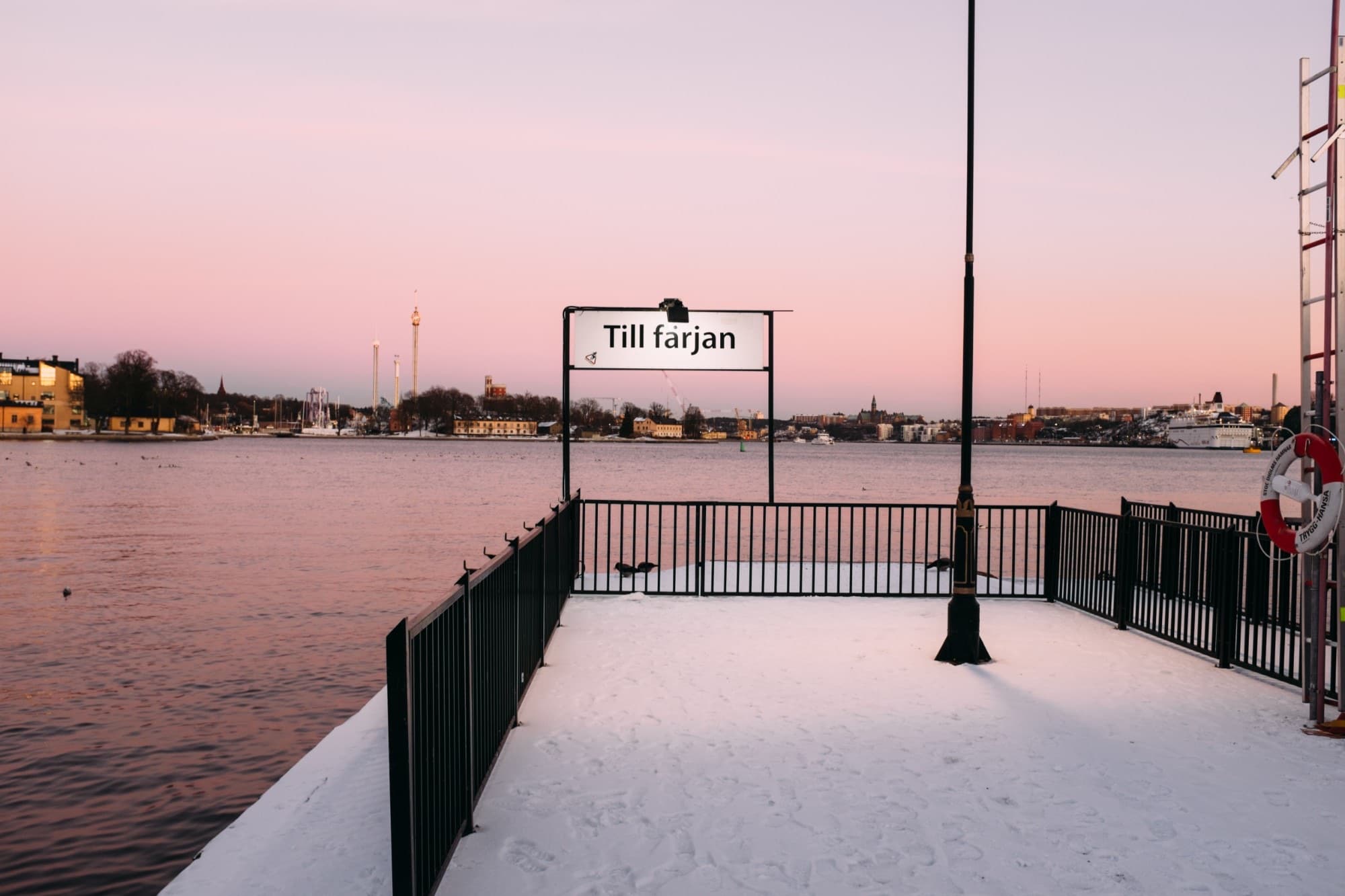 A snowy ferry pier in Stockholm at dusk, with the city across the water